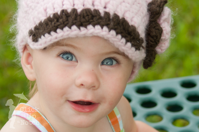 Child with a pink and brown hat on and blue eyes.